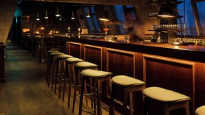 Eine Barbereich mit Holzhockern und einer Bar, ausgestattet mit verschiedenen Flaschen und Gläsern.