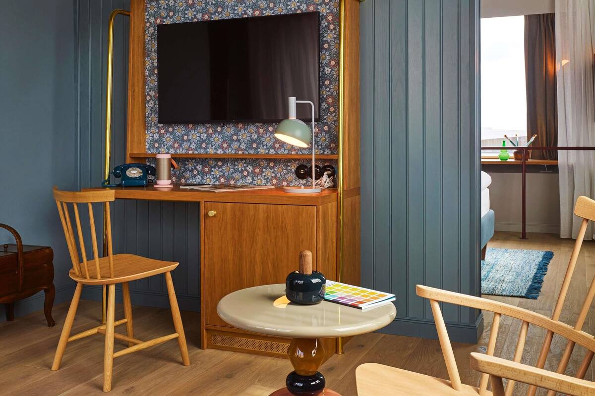 A compact room with a desk, two chairs, a small table, a mirror, and a window with curtains.