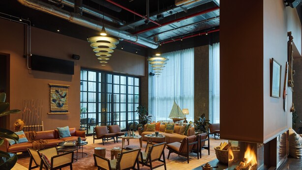 A spacious lounge area with leather sofas, wicker chairs, and a central fireplace. - 25hours Hotel Paper Island (Copenhagen)