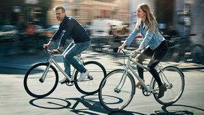 Zwei Personen fahren auf Fahrrädern eine Stadtstraße entlang.