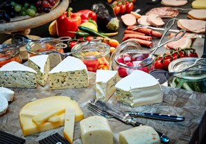 Eine Auswahl an Käse und Wurstwaren auf einem Holzbrett, mit Messer und Gabel in der Nähe.
