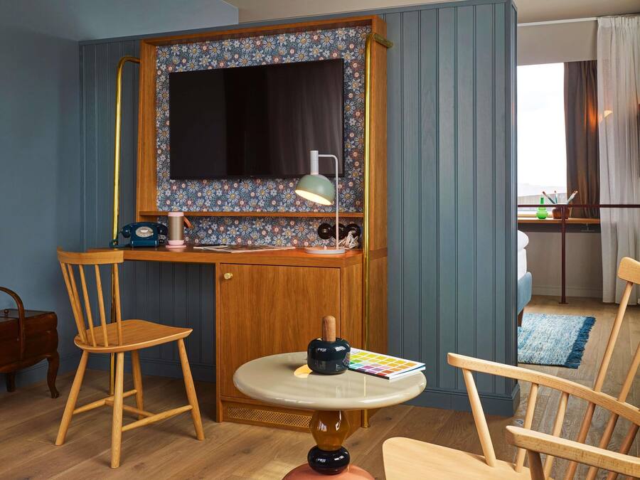 Une pièce de taille modeste, comprenant un bureau, deux chaises, une petite table, un miroir et une fenêtre avec des rideaux.