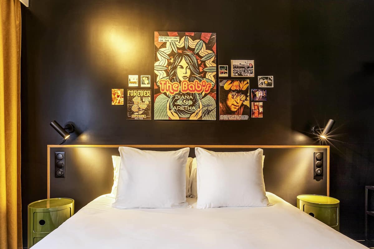 A hotel room with a large bed, two bedside tables, a wall with framed pictures, and a curtain.