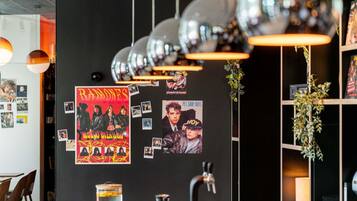 Een muur met diverse posters en foto's, een bar met flessen, en een hangende lamp.