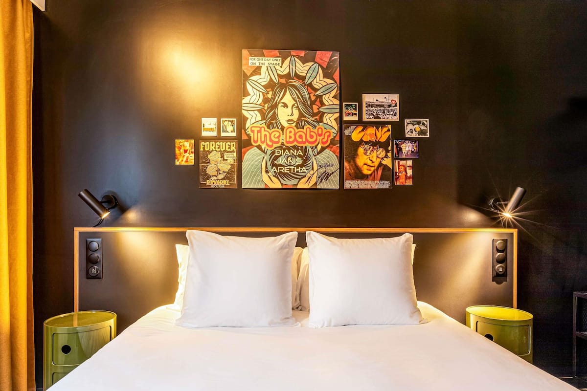 Habitación de hotel con una cama grande, dos mesitas de noche y una pared decorada con carteles y fotografías.