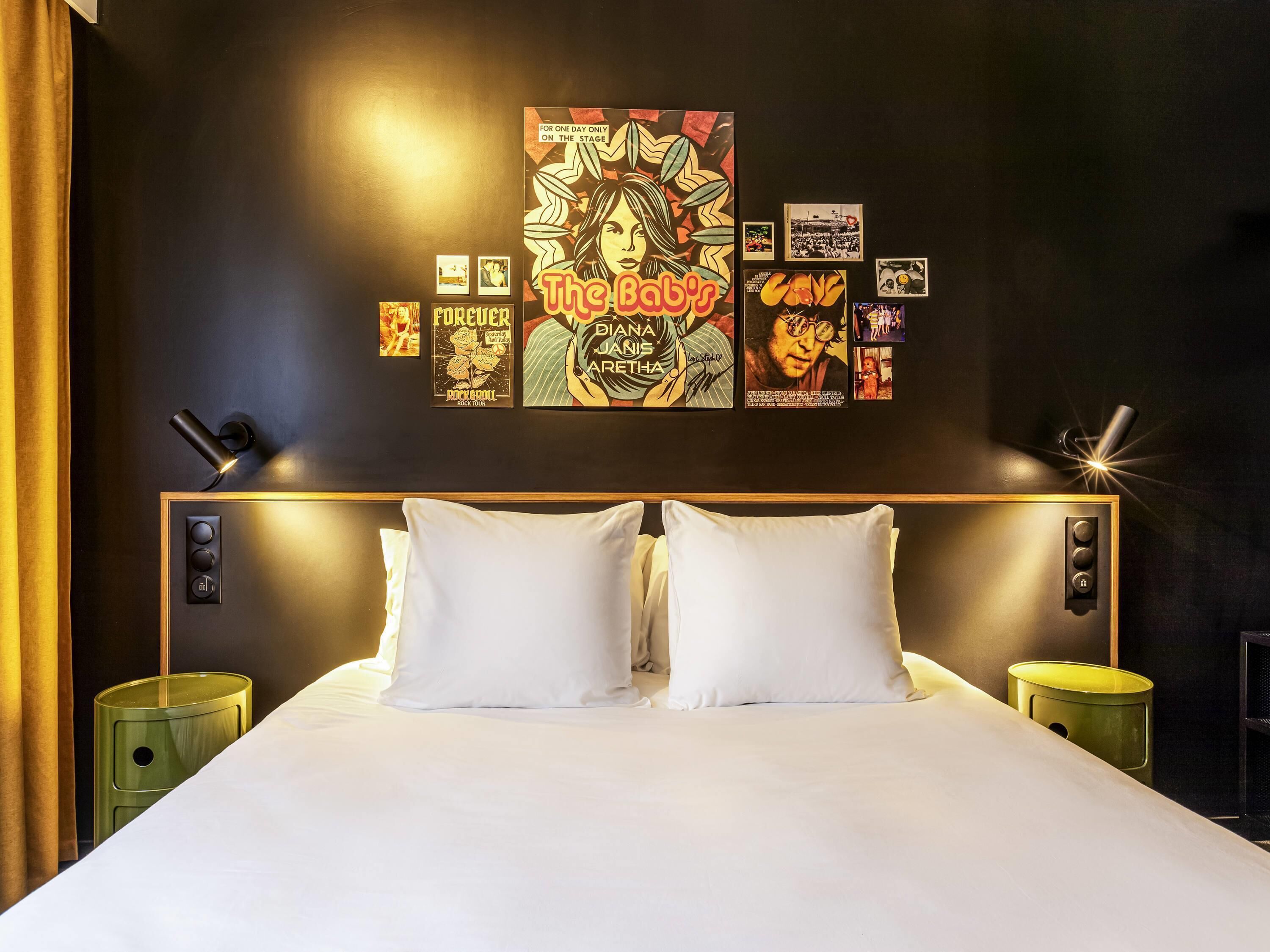 Een hotelkamer met een groot bed, twee nachtkastjes, een muur met ingelijste foto’s en een gordijn.