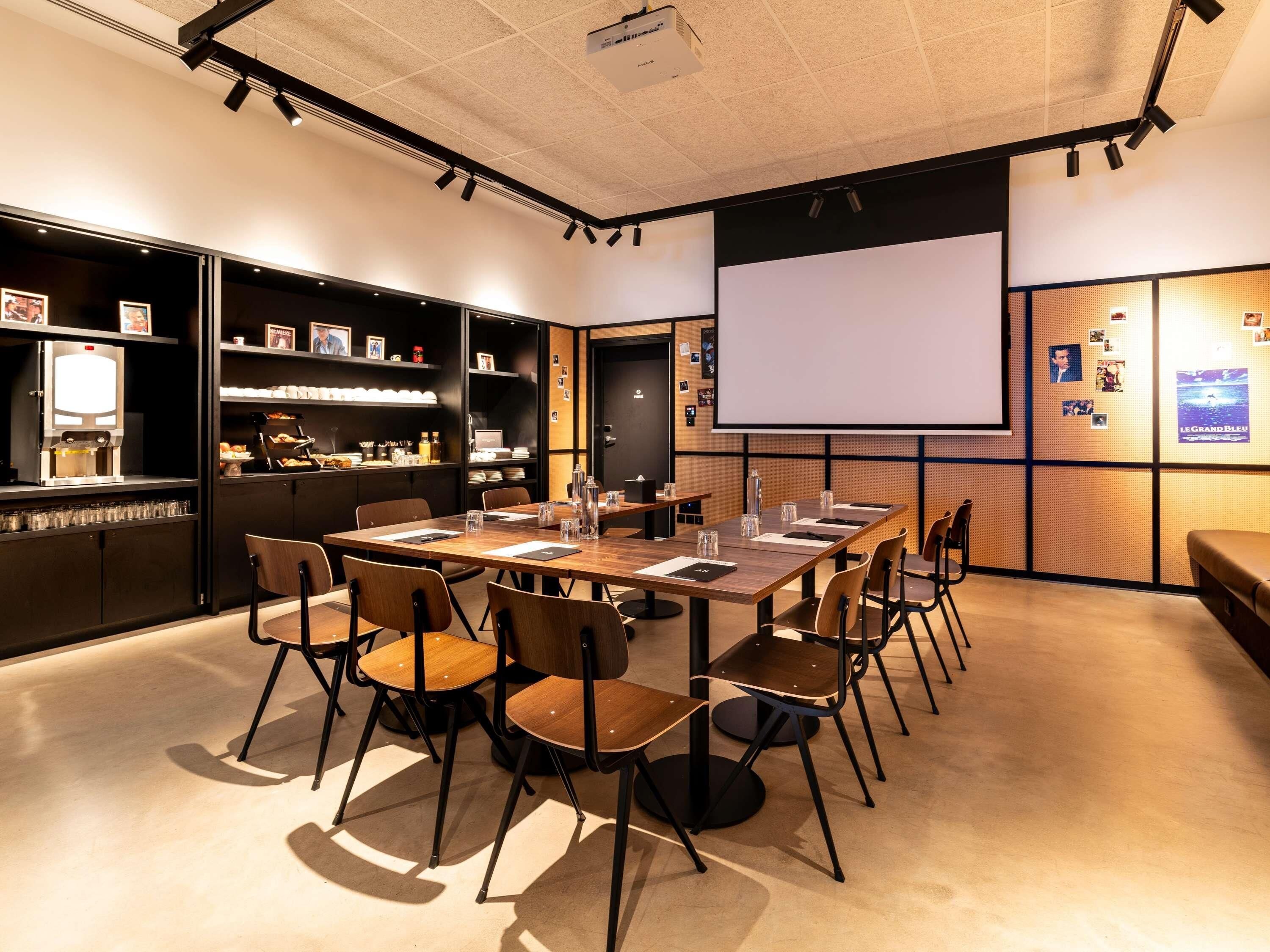 A conference room with a large table, chairs, a projector screen, and a coffee machine.