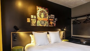 Een hotelkamer met een groot bed, hoofdeinde, een wandtelevisie en een groene prullenbak.