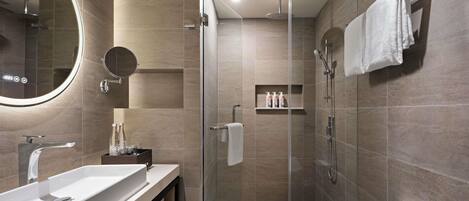 Un baño moderno con ducha envuelta en vidrio, un espejo grande y un tocador con lavamanos.