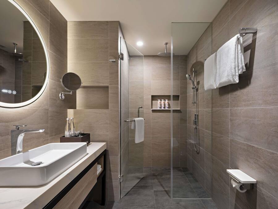 Un baño moderno con ducha envuelta en vidrio, un espejo grande y un tocador con lavamanos.