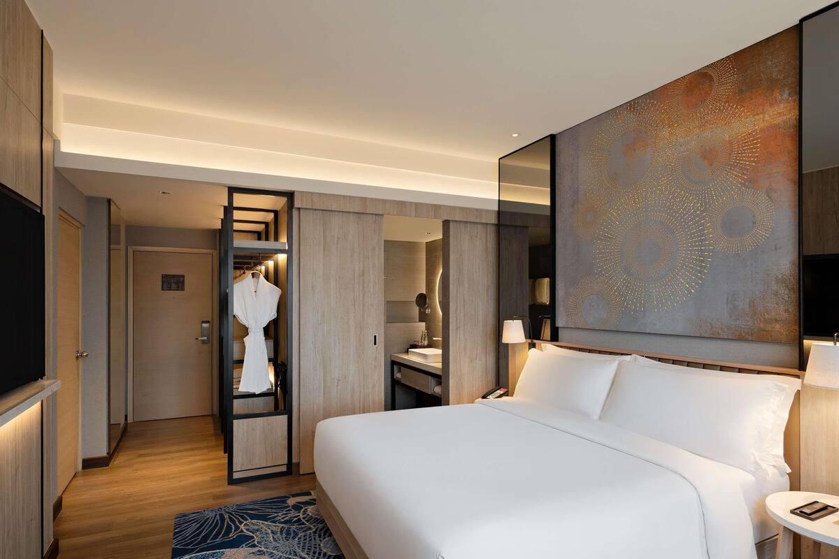 Une chambre d’hôtel moderne dotée d’un grand lit, d’un dressing, d’une salle de bain et d’un grand tableau abstrait accroché au mur.