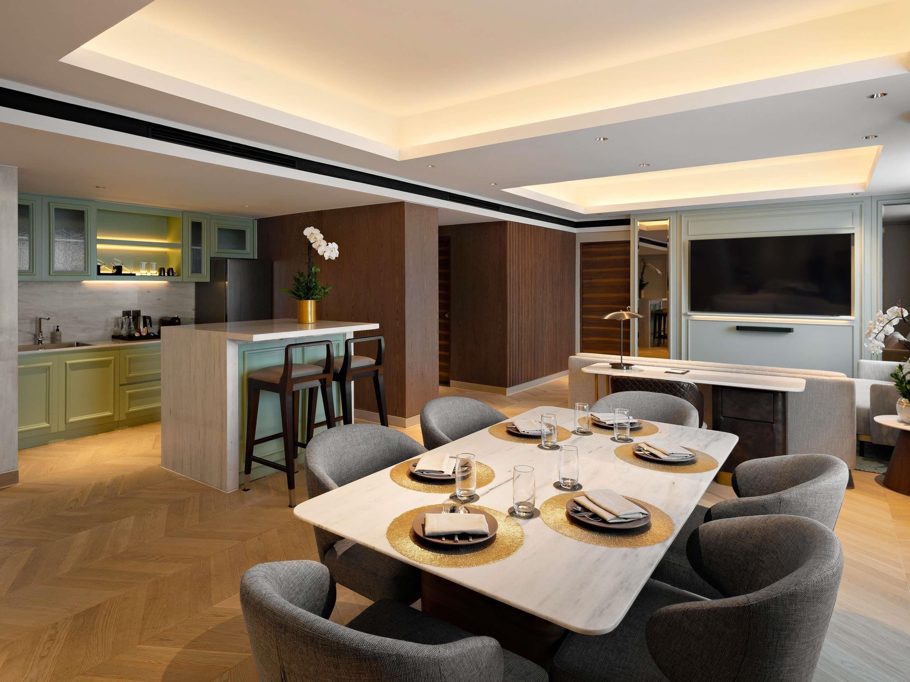 Una cocina moderna con una isla central, un comedor con una mesa grande y sillas, y un televisor en la sala.