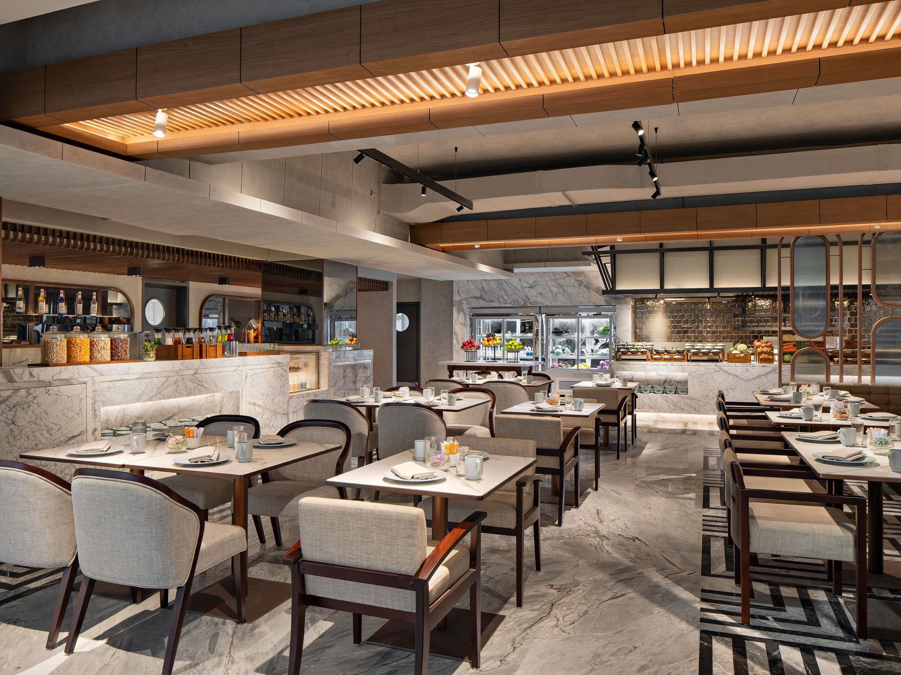 A modern restaurant interior with marble flooring, wooden furniture, and a bar area with various food displays.