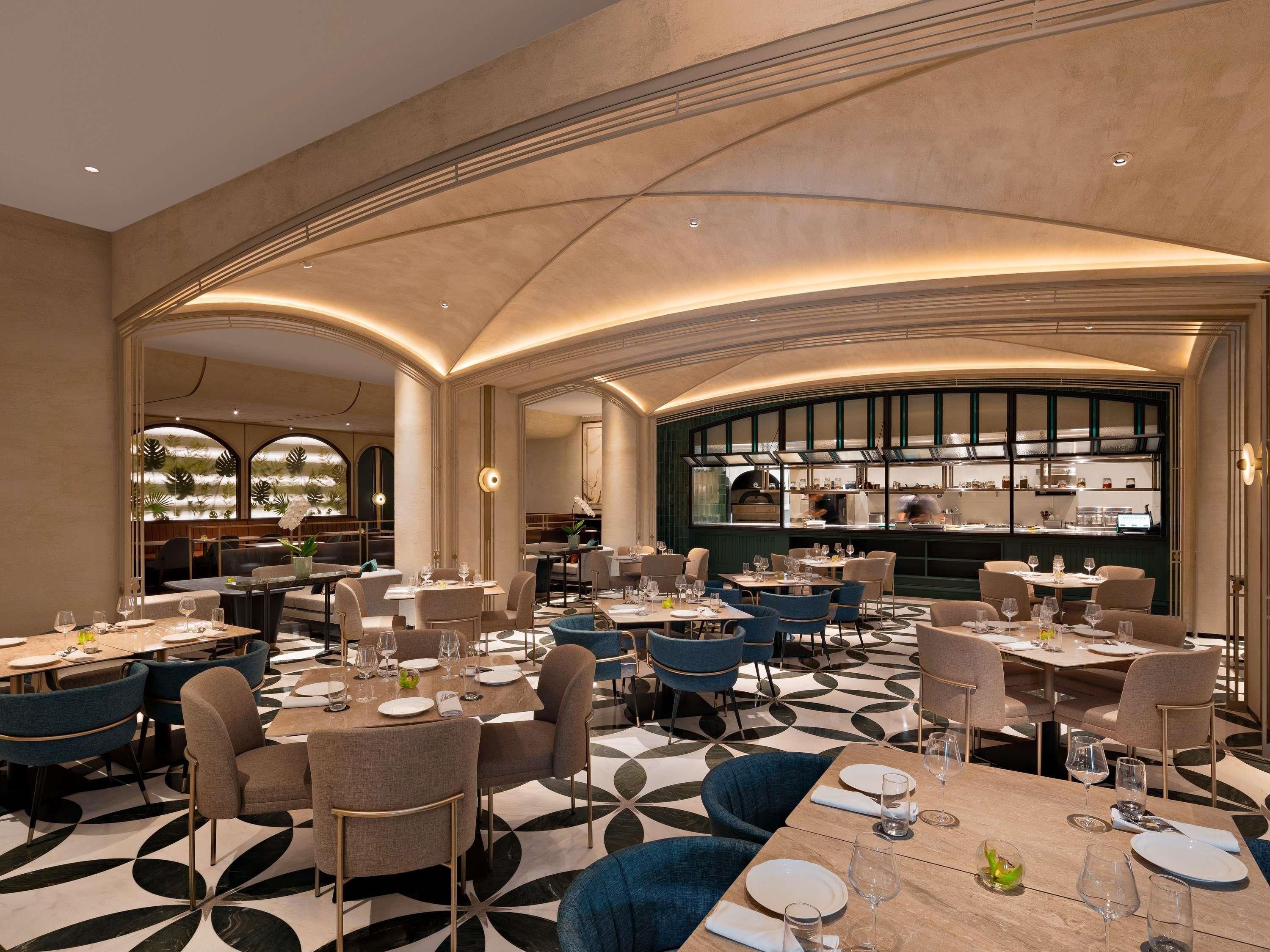 A modern restaurant with a geometric floor pattern, curved ceiling, and a central bar area.