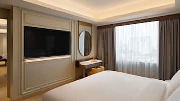 Une chambre d’hôtel avec un grand lit, un téléviseur fixé au mur, un petit bureau avec un miroir et une fenêtre avec des rideaux.