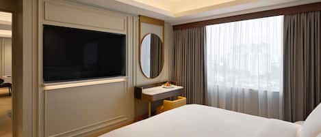 A hotel room with a large bed, a TV mounted on the wall, a small desk with a mirror, and a window with curtains.