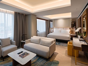 A hotel room with a bed, a sofa, a desk, a chair, a coffee table, and a large window with curtains.