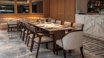 Un comedor moderno con una mesa larga dispuesta para varias personas, paneles de madera en las paredes y suelo de mármol.