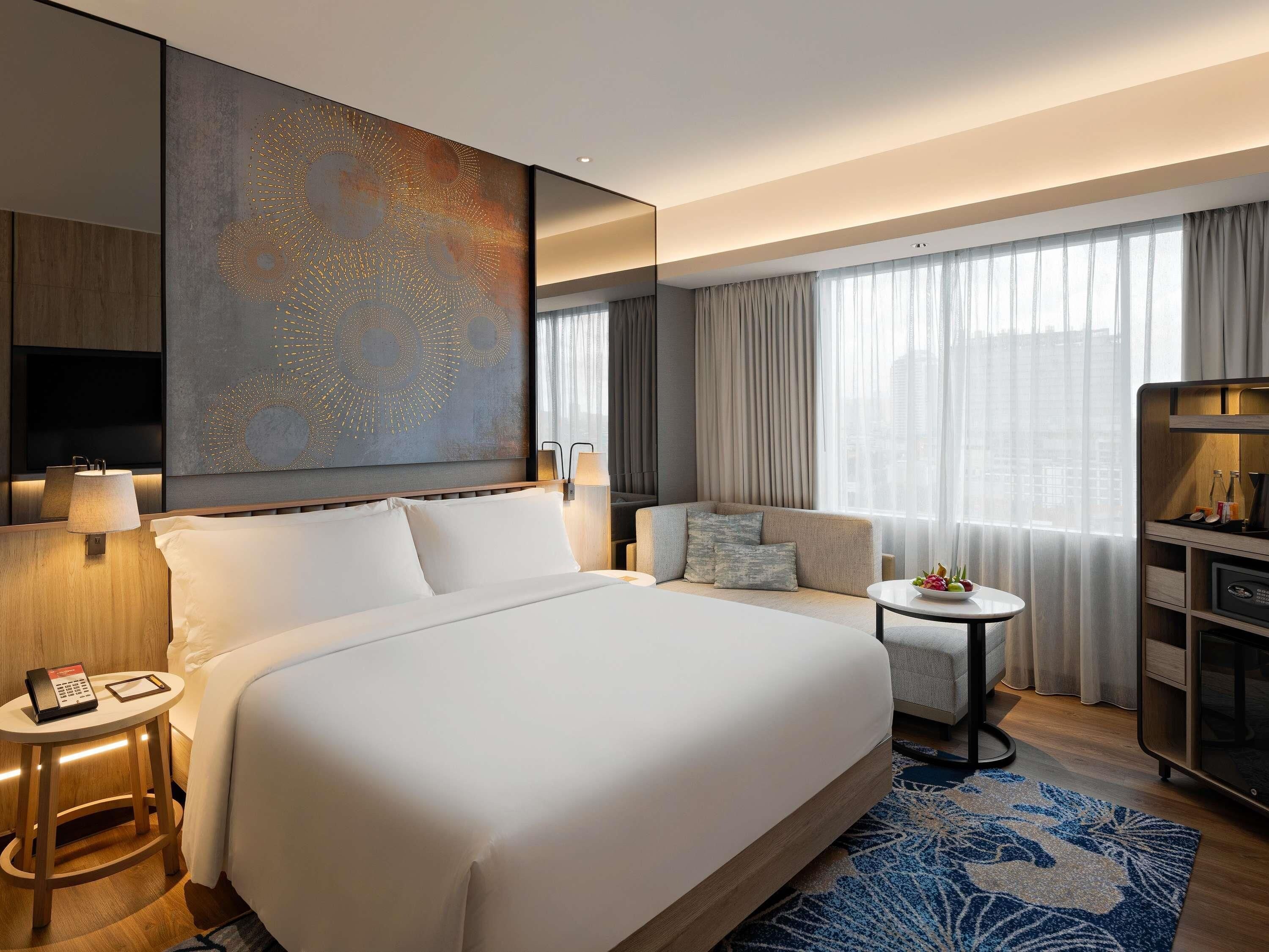 Habitación de hotel con una cama grande, un sofá, una mesita, un televisor y un minibar.
