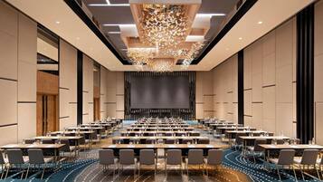 A conference room with a stage, multiple tables, and chairs, and a decorative ceiling light fixture.