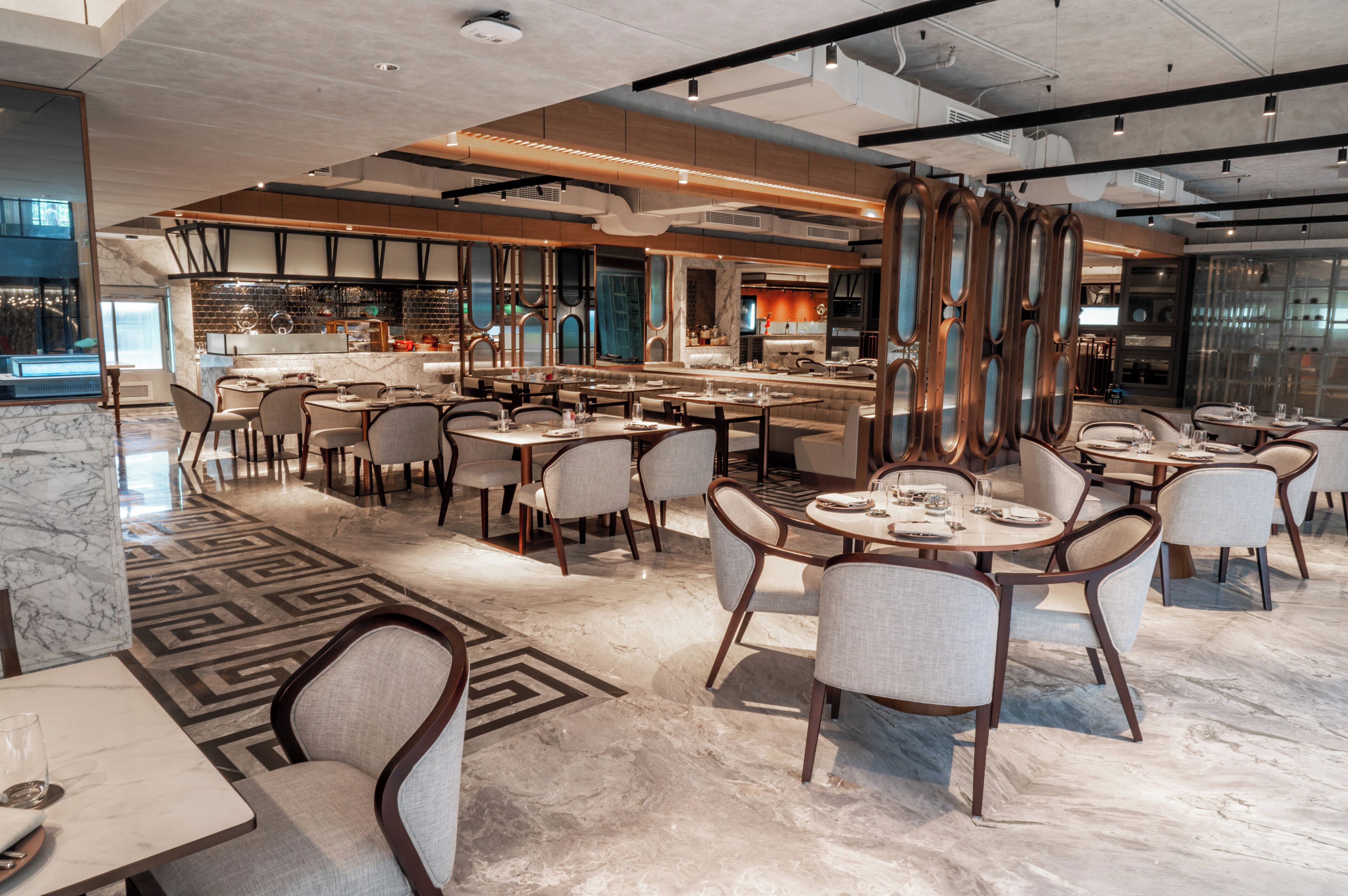A modern restaurant with marble flooring, multiple dining tables and chairs, and a kitchen area visible in the background.