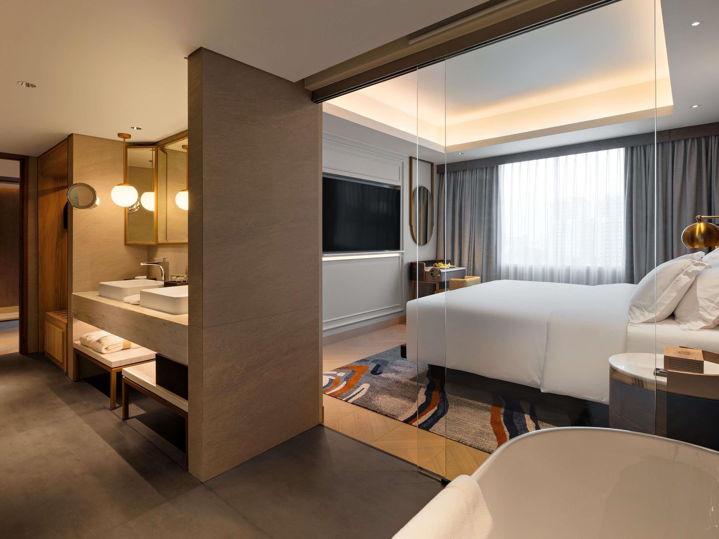 Une chambre d’hôtel moderne dotée d’un grand lit, d’une salle de bain séparée avec un meuble-lavabo, d’un grand miroir et d’une télévision.