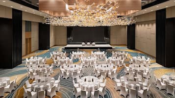 A large conference room with round tables and white chairs, a stage, and a patterned carpet.