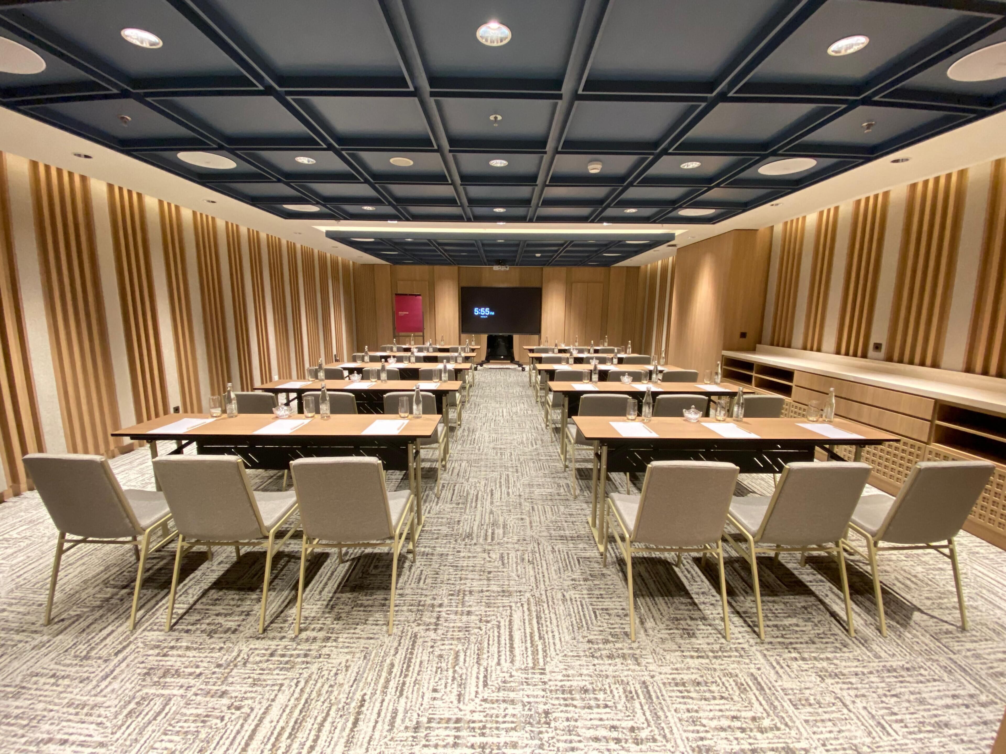 A conference room with multiple tables and chairs, a large screen, and a patterned carpet.