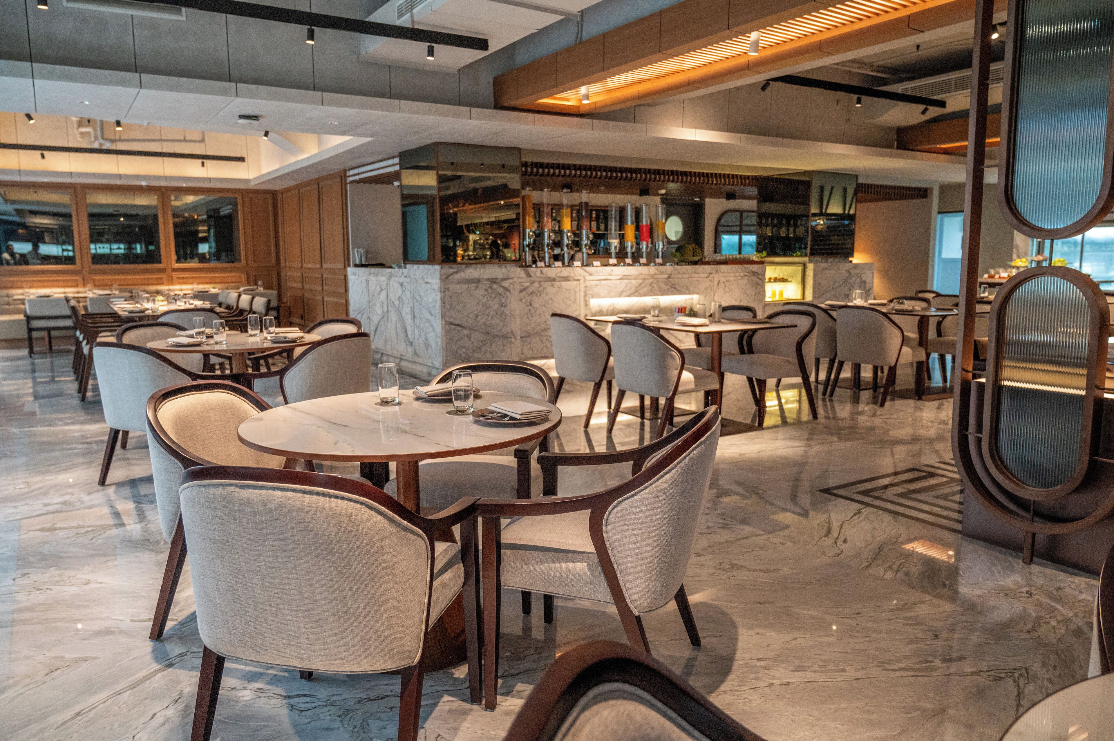 Un restaurant moderne doté d’un sol en marbre, de tables en bois et de chaises rembourrées.