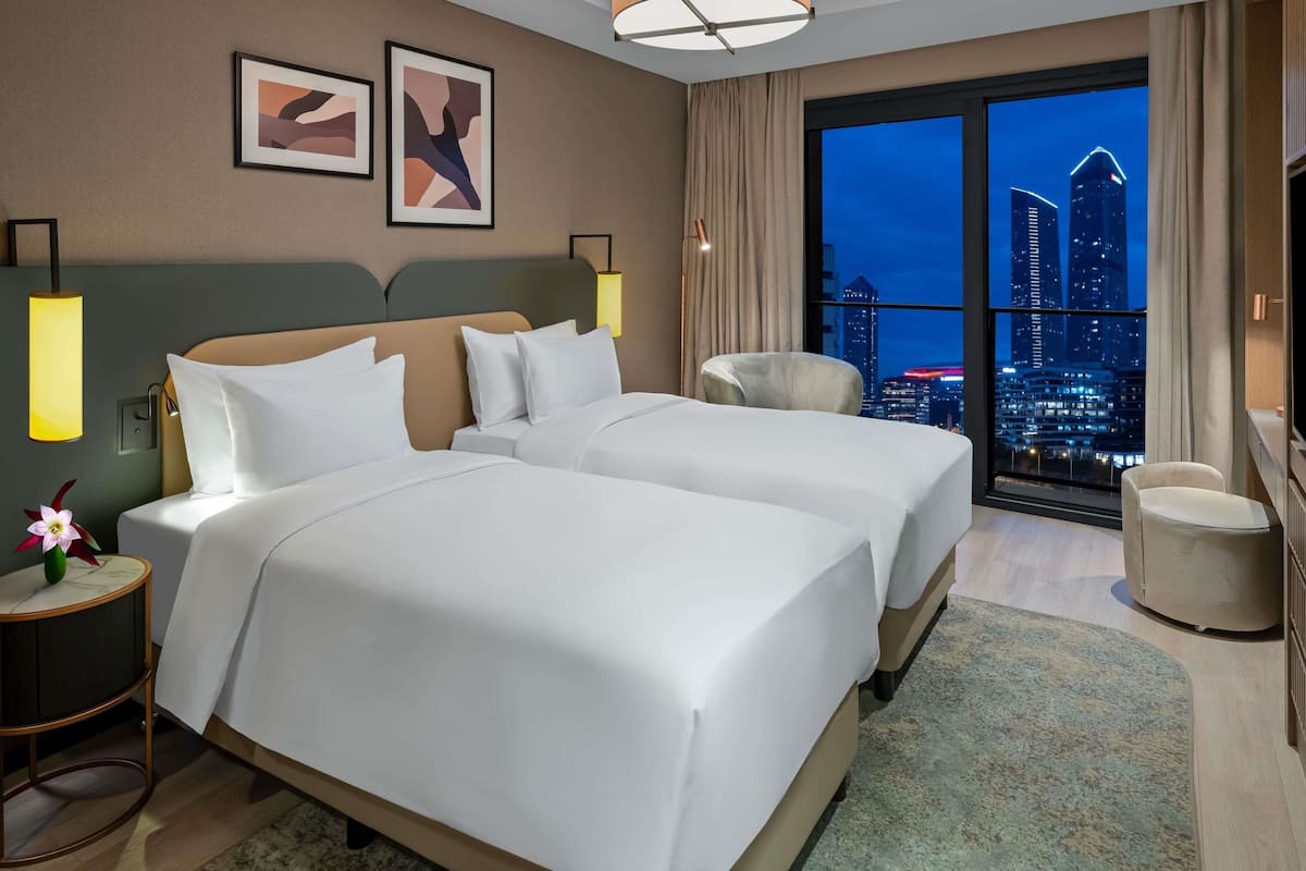 Een hotelkamer met twee bedden, uitzicht op de stad, een lamp en een stoel.