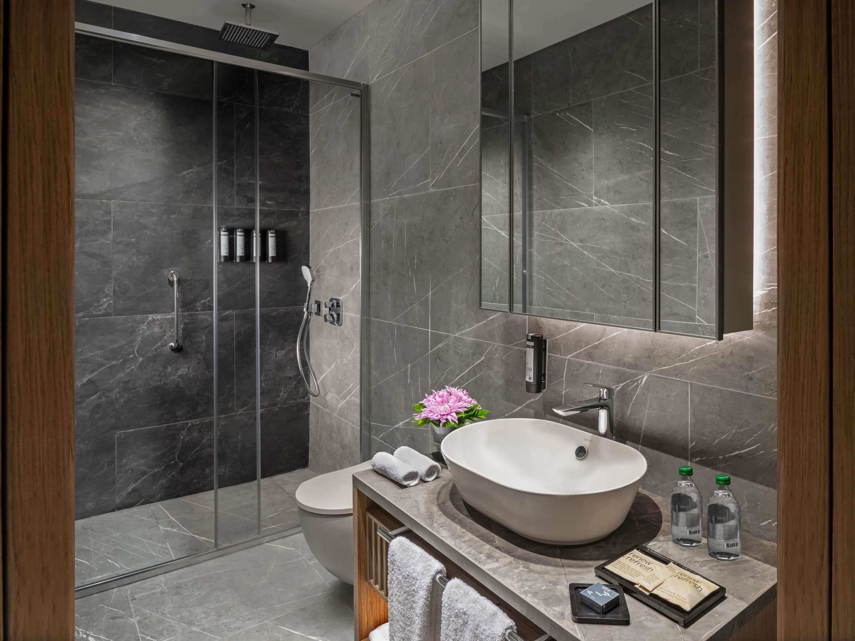Un baño moderno con ducha envuelta en vidrio, inodoro independiente y tocador con un lavamanos de diseño.