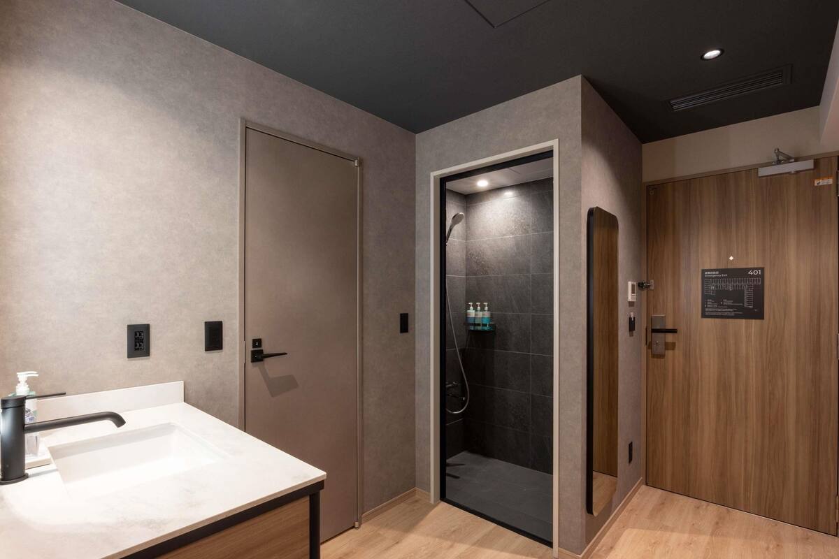 A modern bathroom with a sink, a shower, and a wooden door.