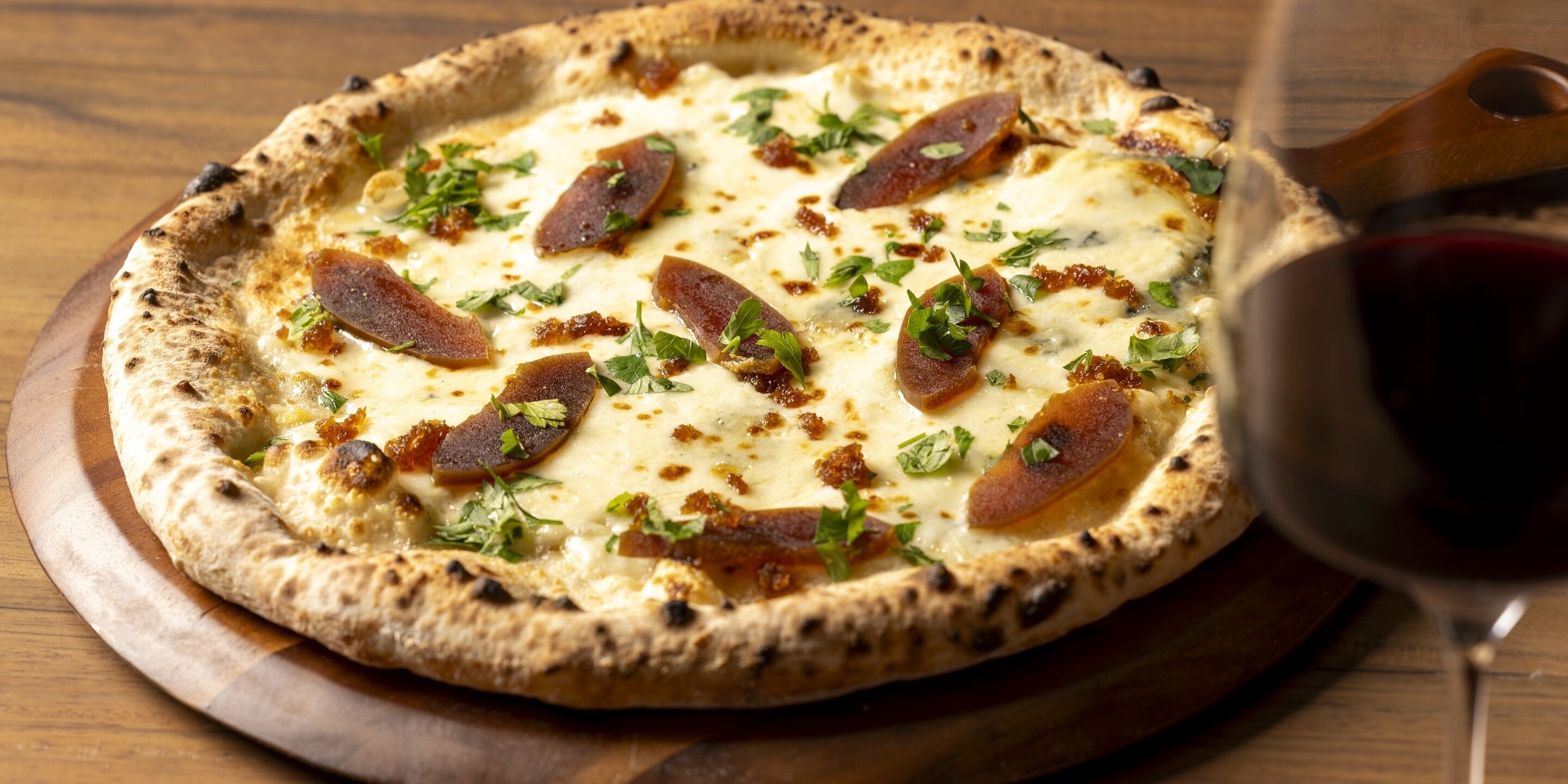 A pizza with cheese, meat, and herbs on a wooden board.