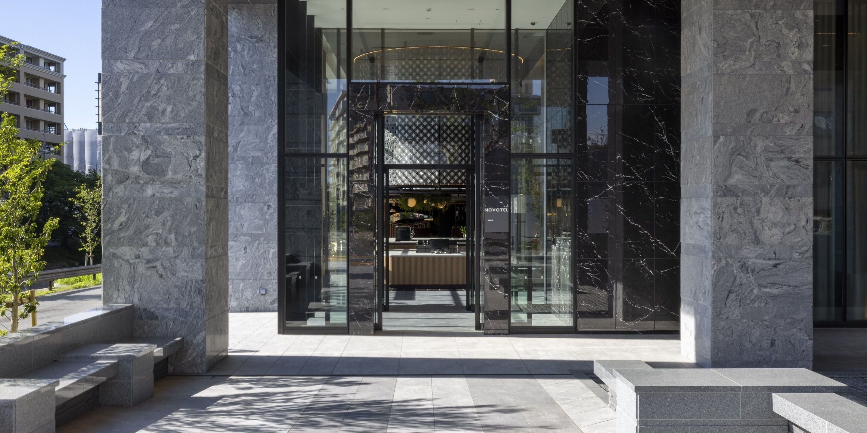 A modern building with large glass doors, a marble facade, and a visible interior with seating and a staircase.