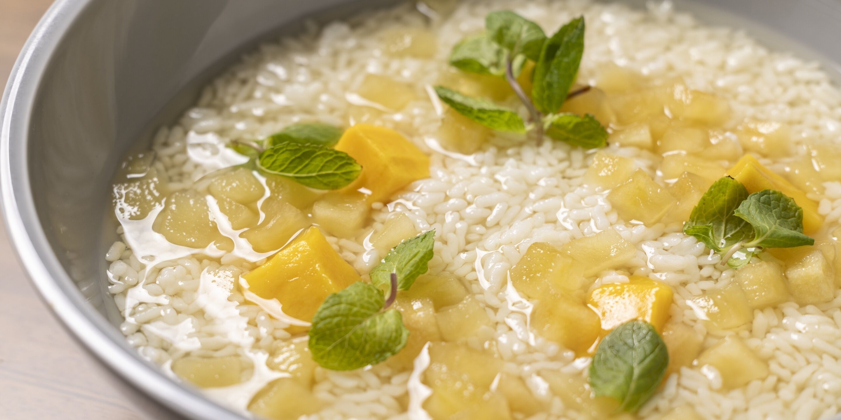 Un bol de riz garni de morceaux de mangue et de feuilles de menthe.