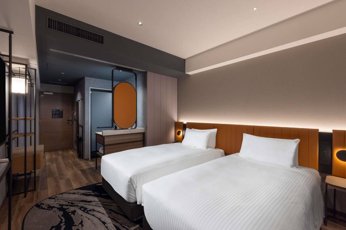 A hotel room with two beds, a desk, a mirror, and a wardrobe.