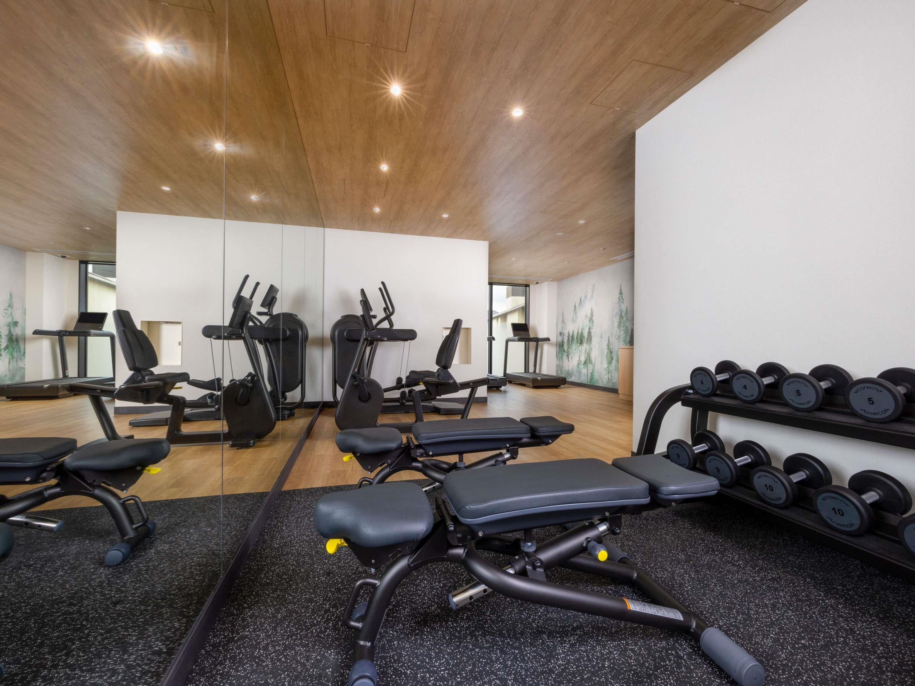 A gym with exercise equipment, treadmills, and a wall with a nature mural.