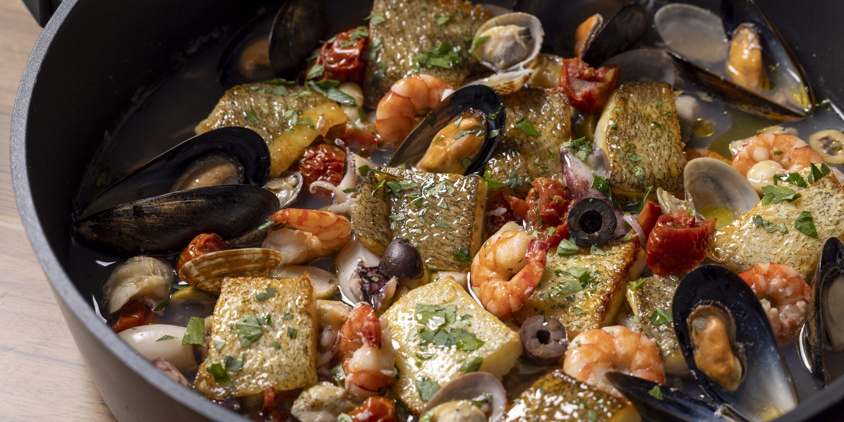 A seafood dish with mussels, shrimp, and fish in a pan.