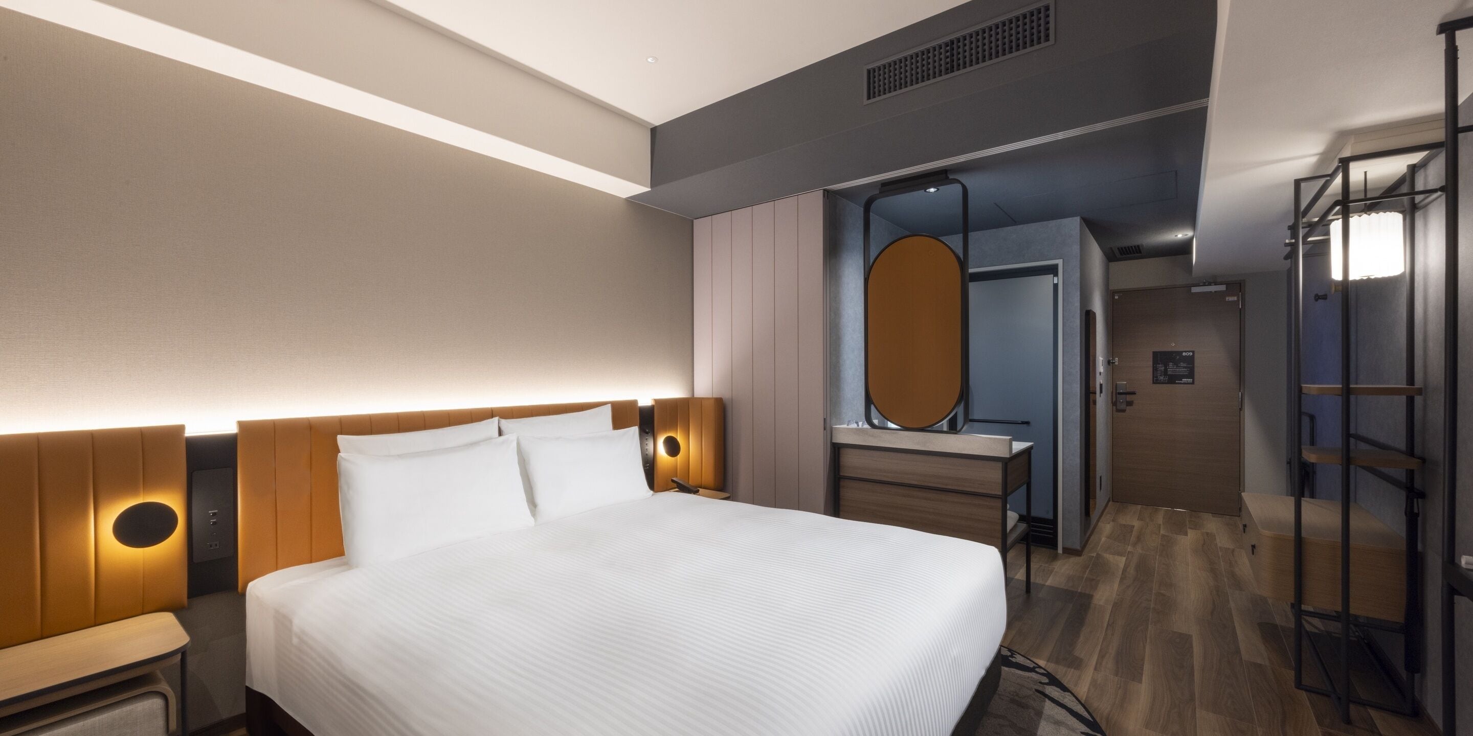 Moderni hotellihuone, jossa on suuri sänky, yöpöydät, peilillä varustettu meikkipöytä ja erillinen vaatehuone.