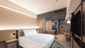 Une chambre d’hôtel moderne dotée d’un grand lit, d’une télévision à écran plat, d’un bureau avec un miroir et d’un dressing.