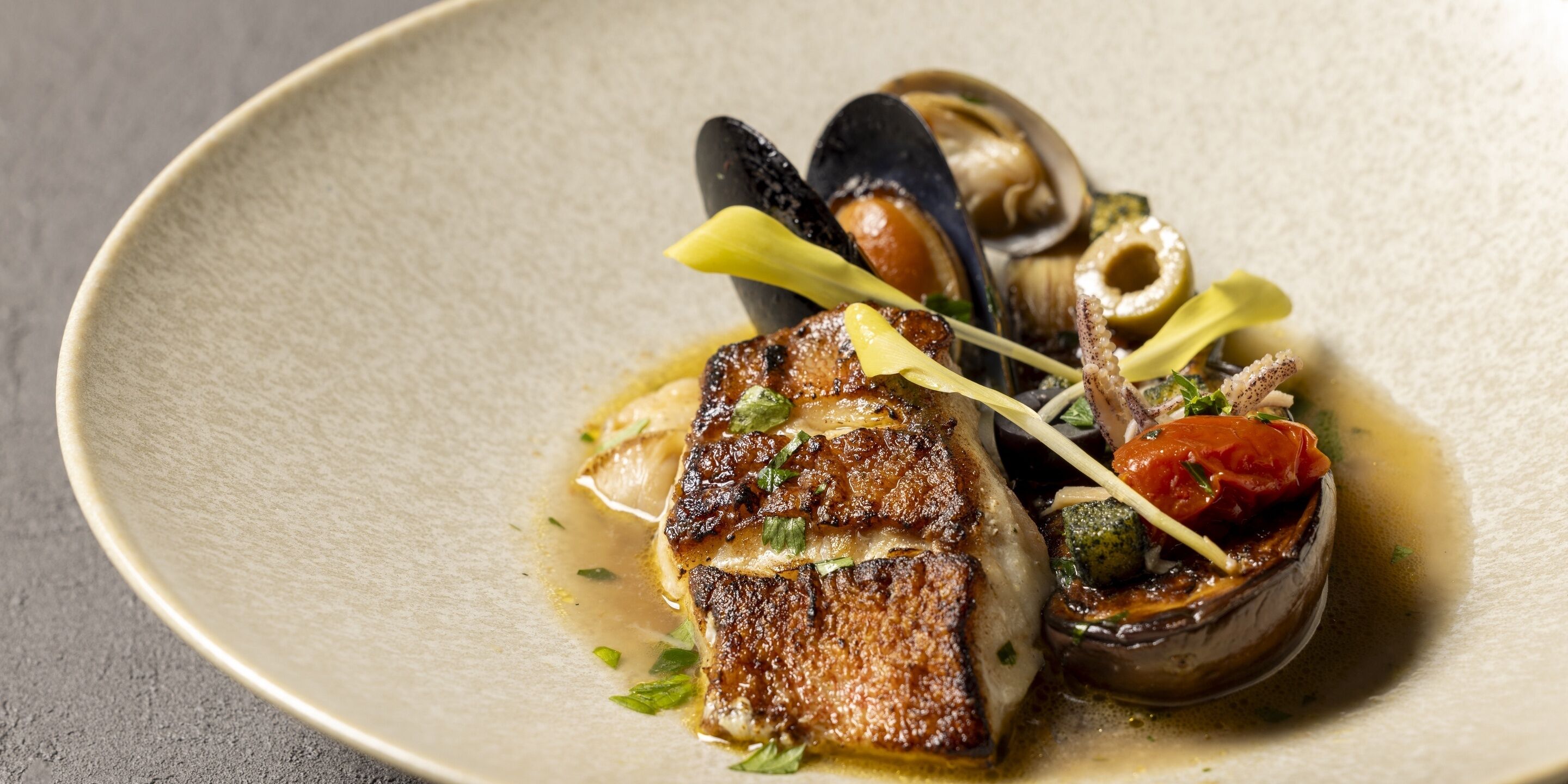 A plate of food with mussels, a grilled fish, and vegetables.