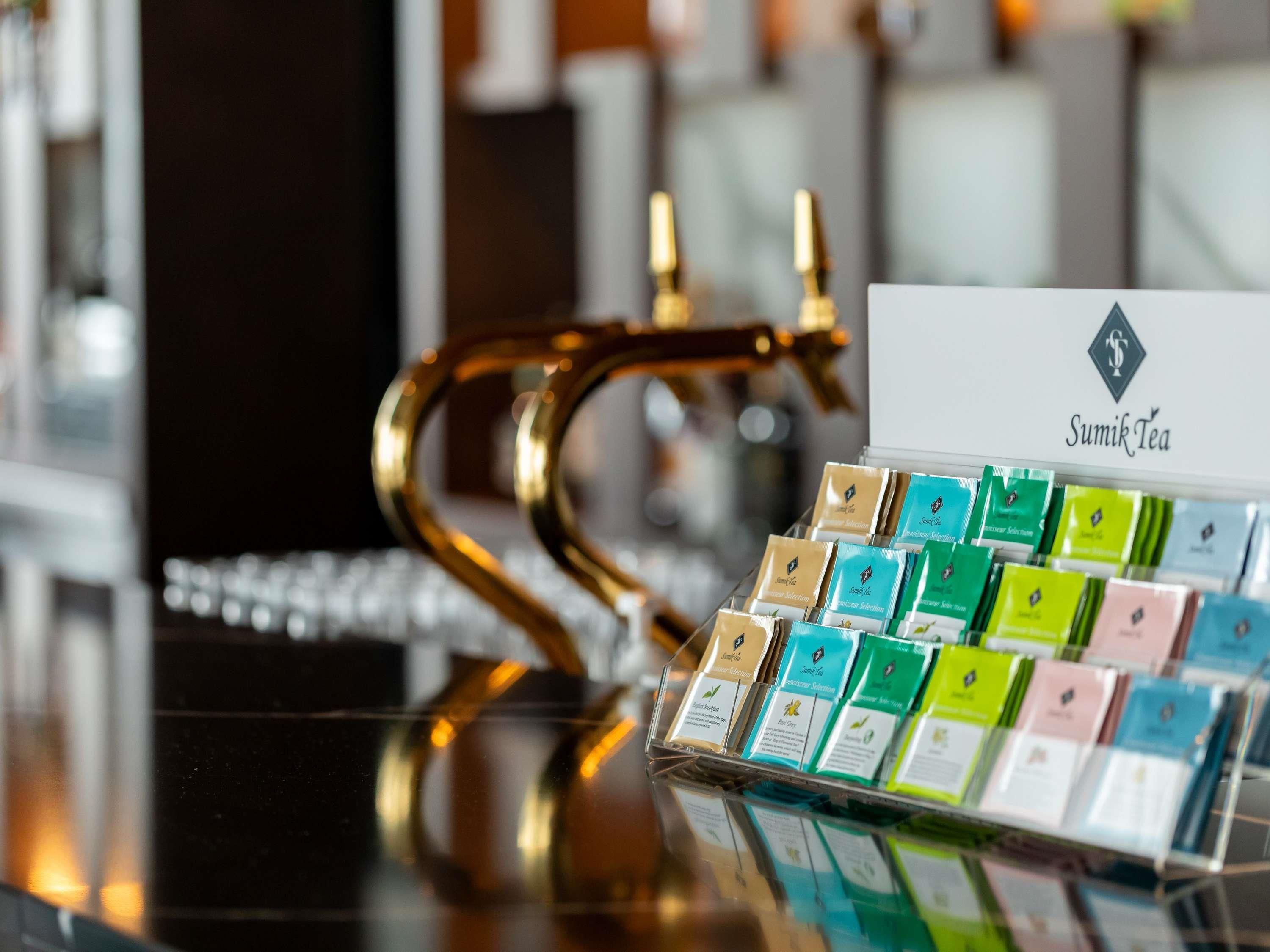 Una presentación de paquetes de té con un letrero que dice 'Sumik Tea' sobre una superficie reflectante.