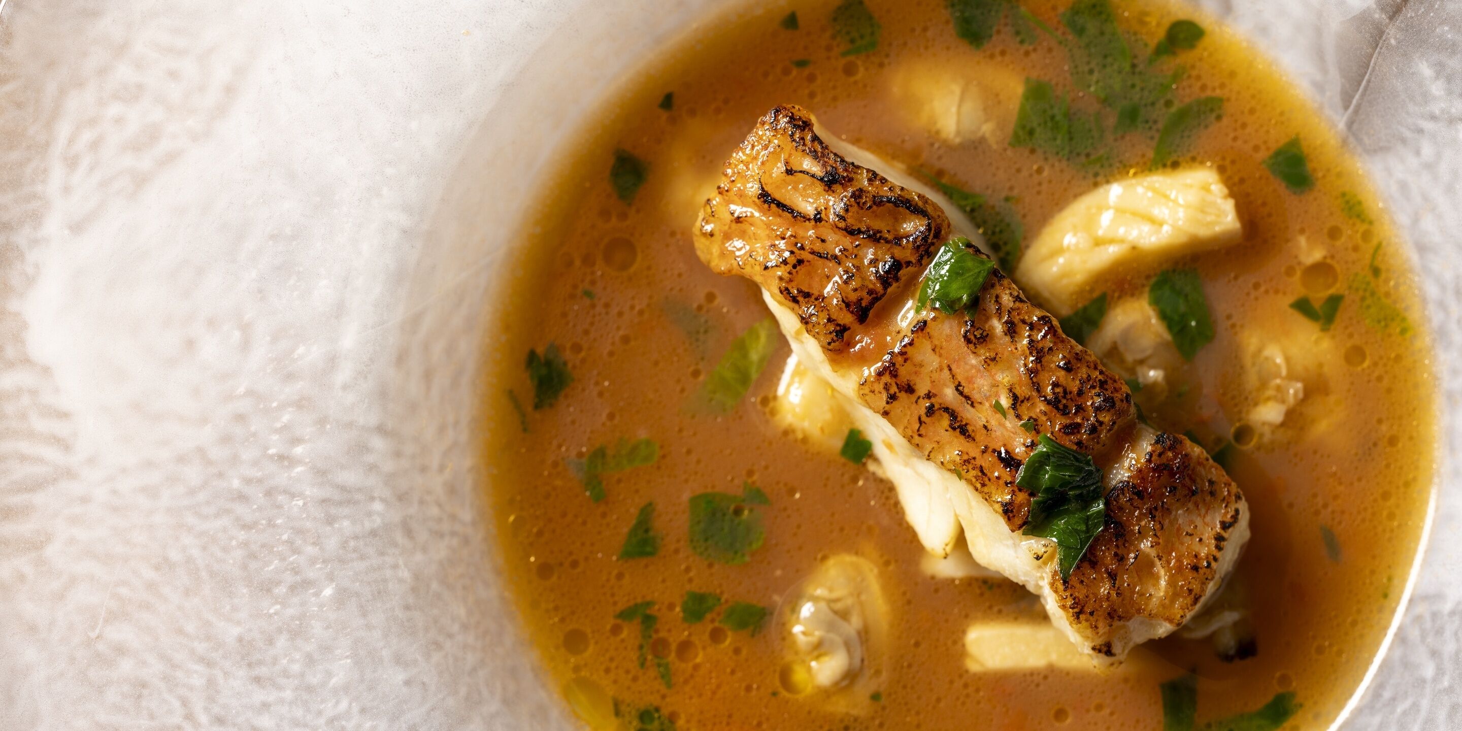 Un tazón de sopa con un trozo de pollo a la parrilla y hierbas.