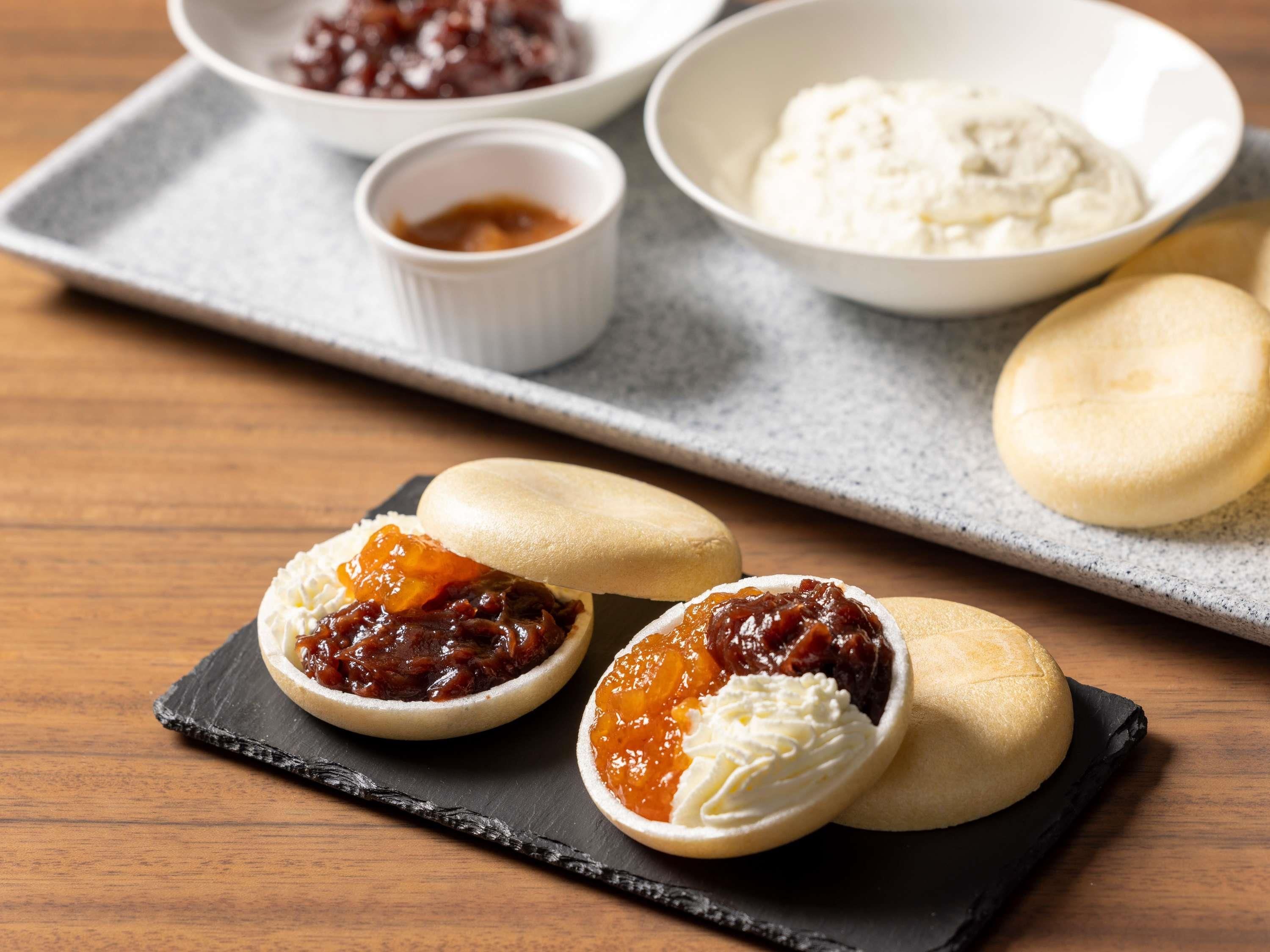 A tray with bao buns, one cut open revealing a filling, and two small bowls of condiments.