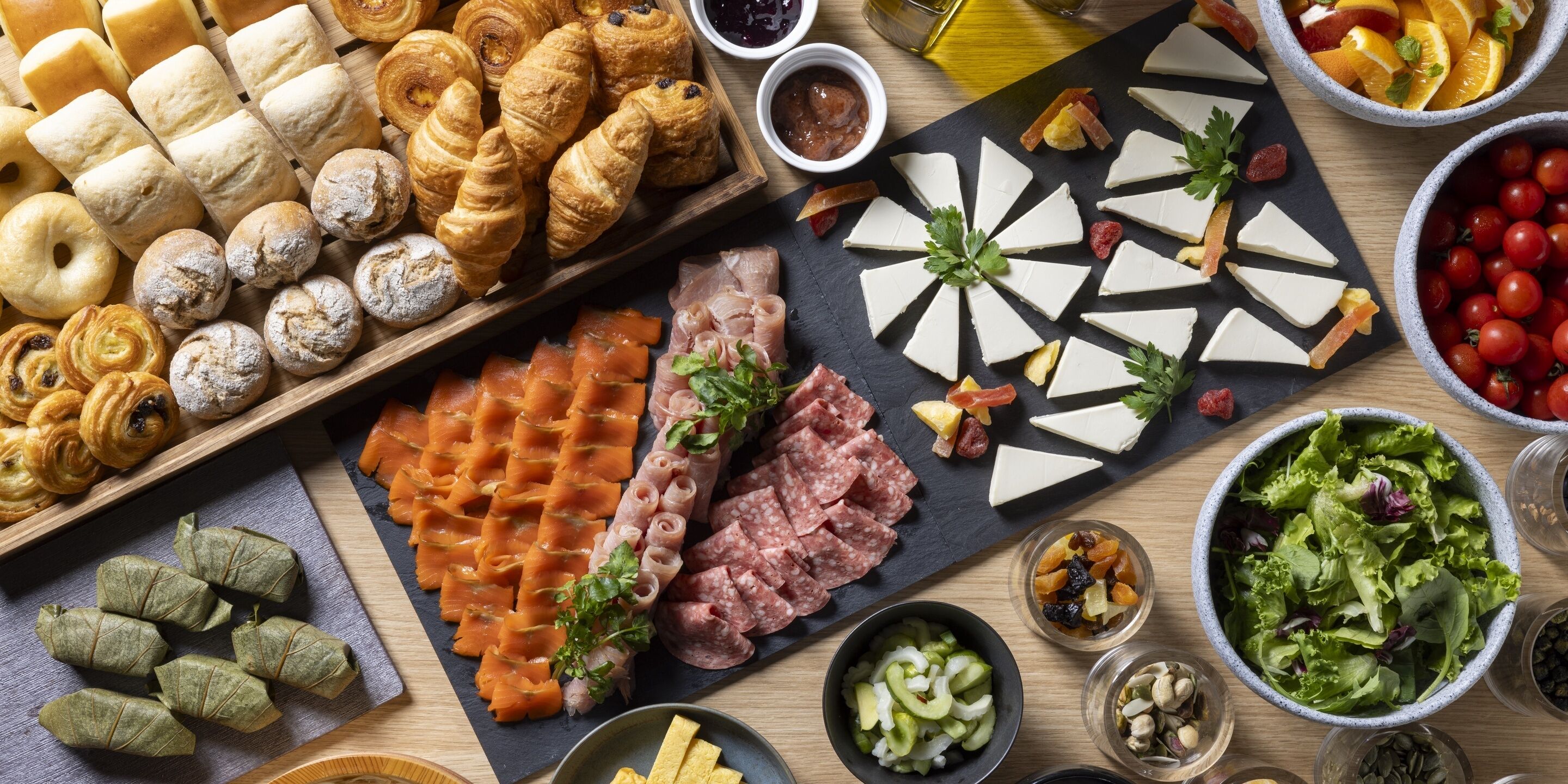 A variety of food items including pastries, meats, cheeses, and salads arranged on a wooden table.