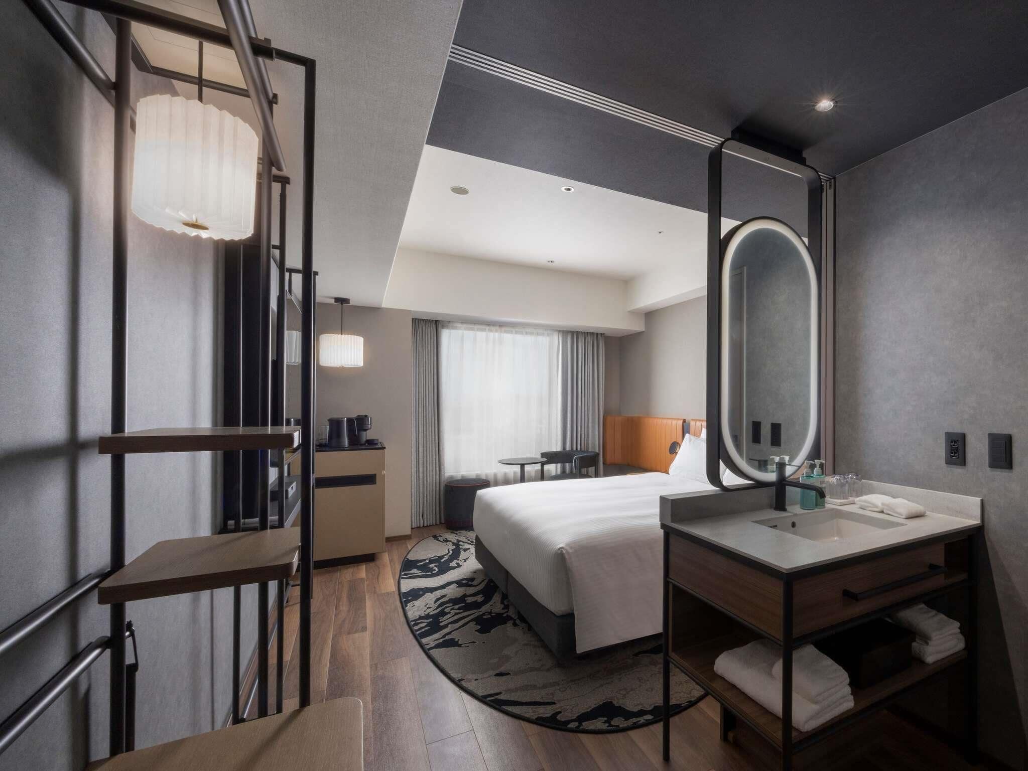 Una habitación de hotel moderna con cama, escritorio, silla, espejo grande, lavamanos y ventana con cortinas.