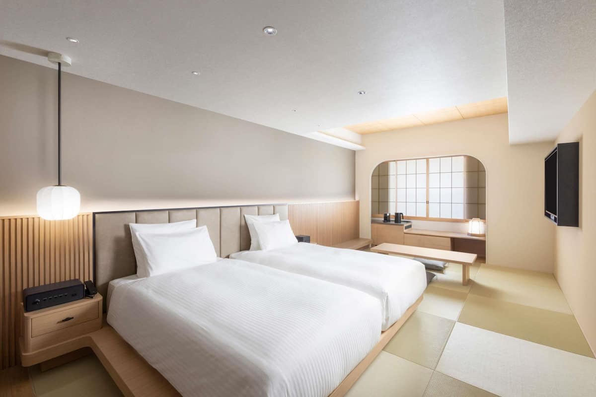 A modern hotel room with a large bed, bedside tables, a vanity with a mirror, and a flat-screen TV mounted on the wall.