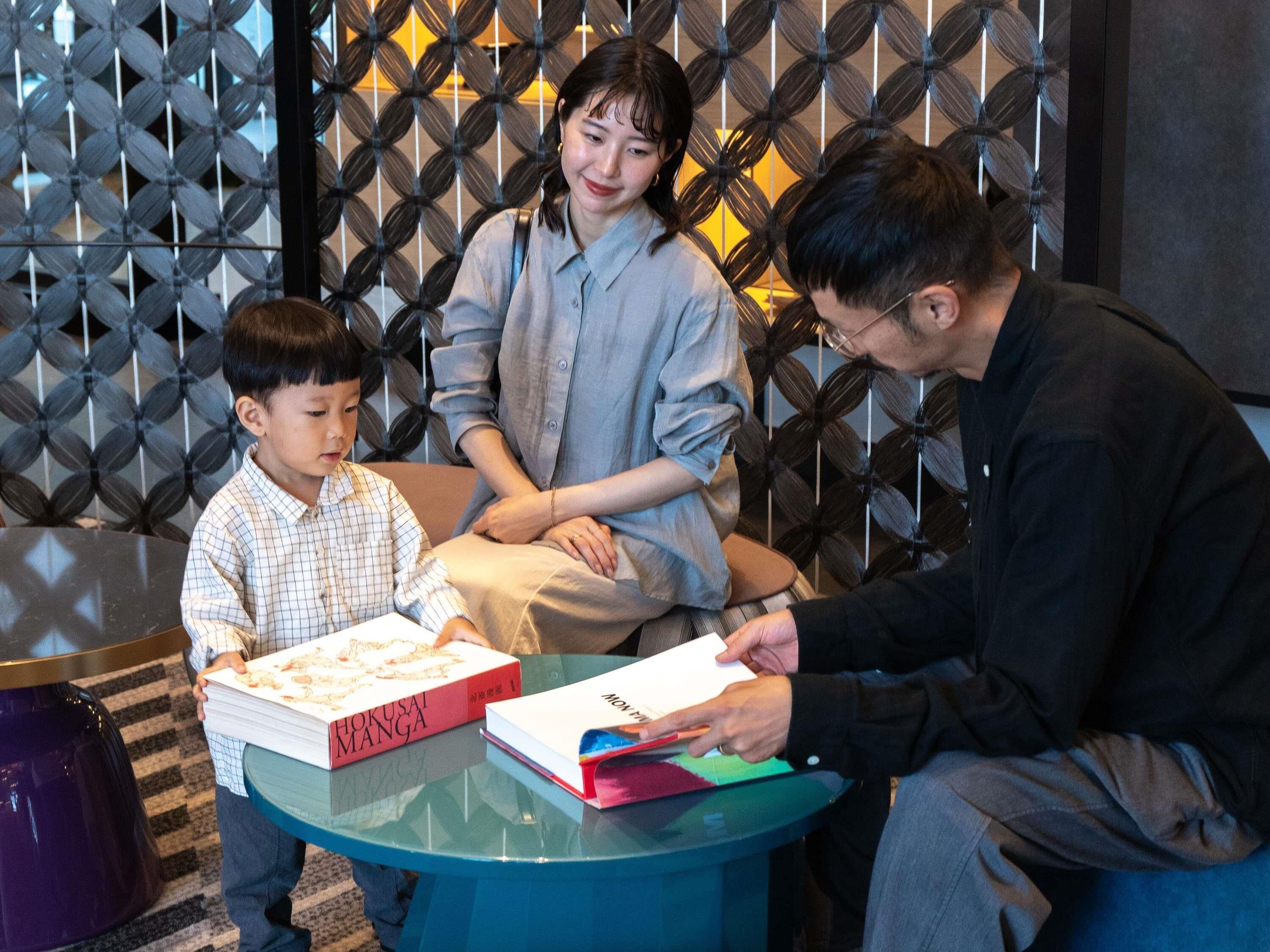A group of people seated around a table with books, in a room with patterned walls.