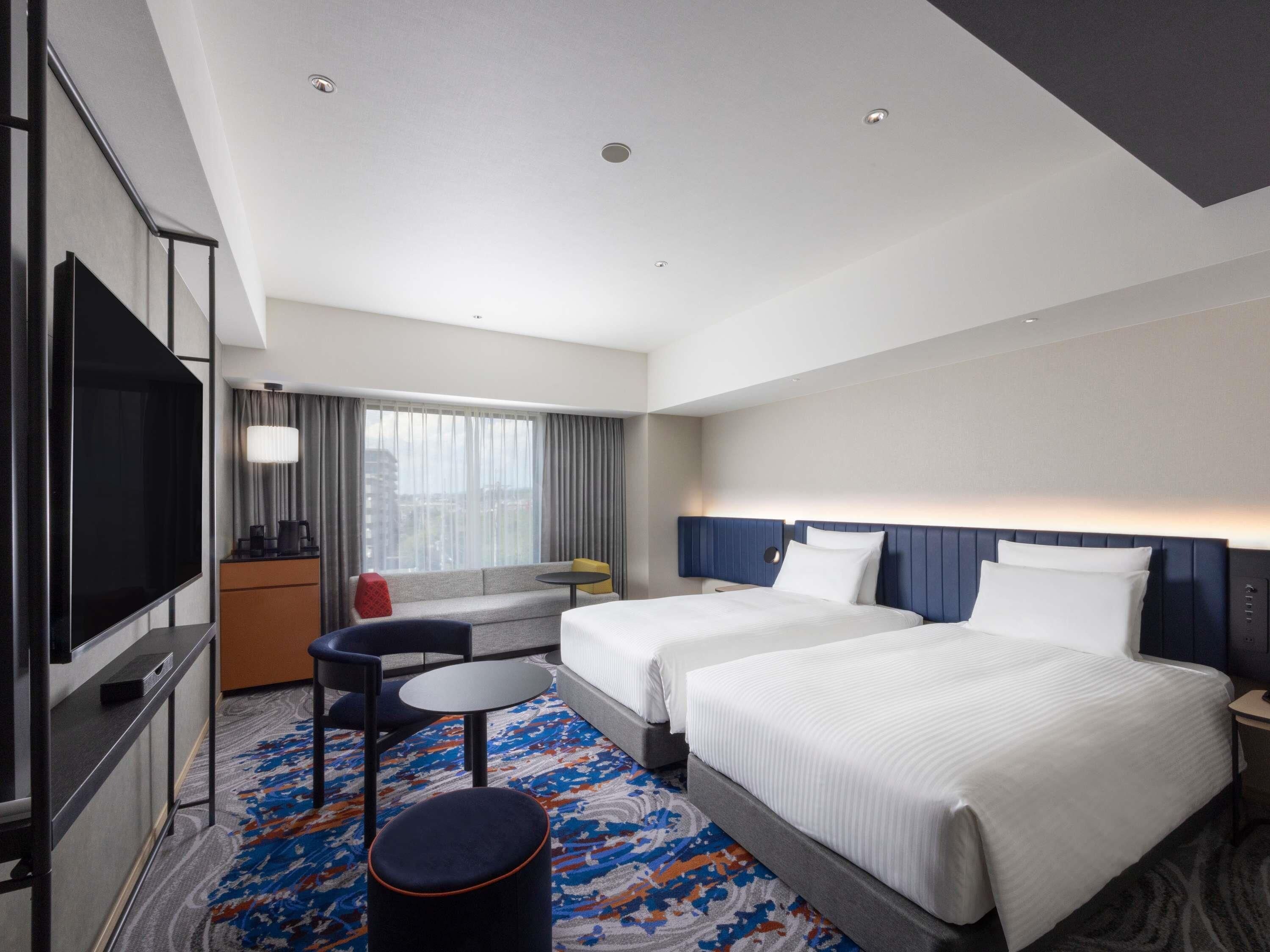 A hotel room with two beds, a TV, a desk, a chair, a small table, and a sofa.