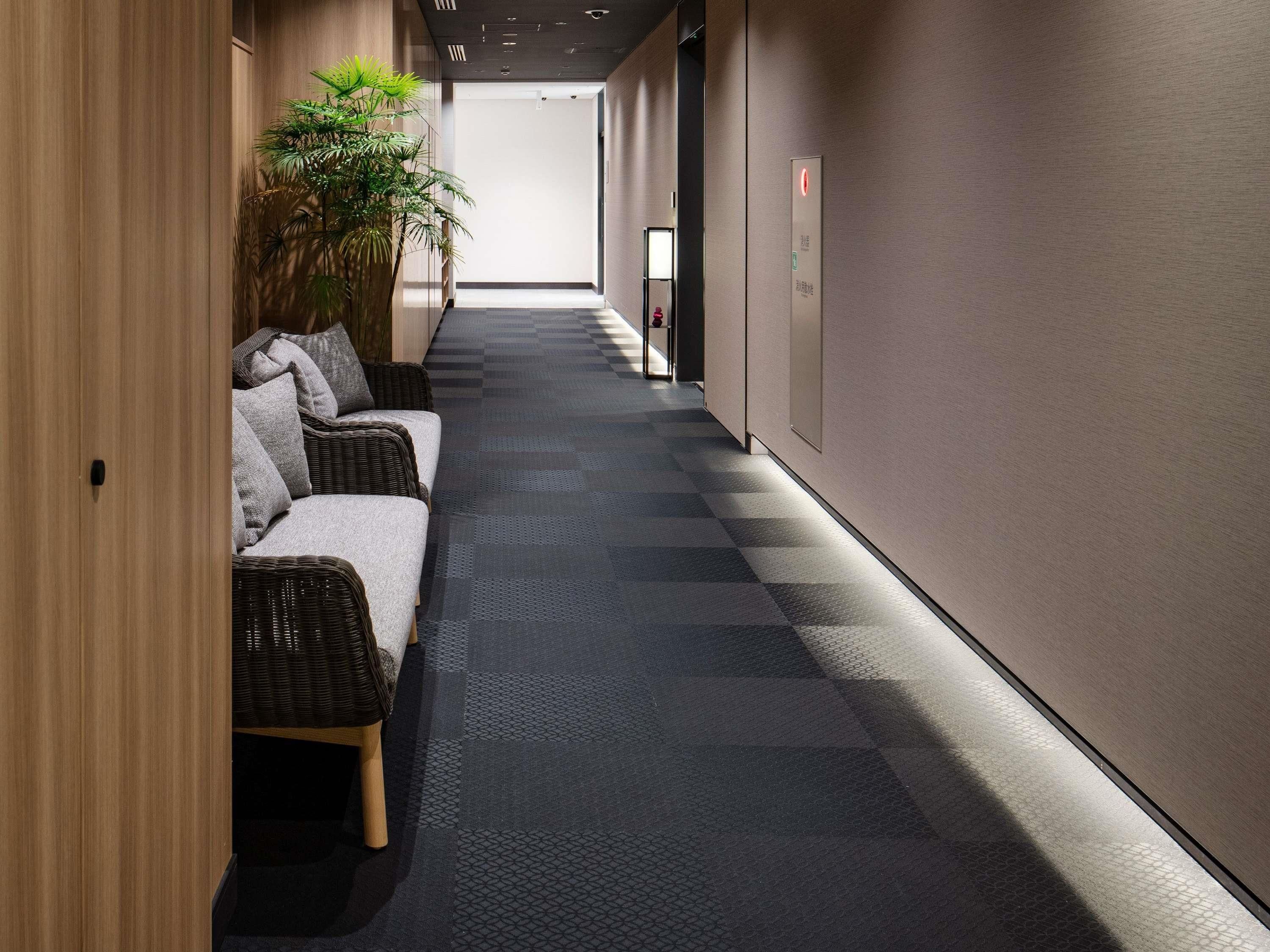 A hallway with a checkered floor, a row of wicker sofas with cushions, and a potted plant.